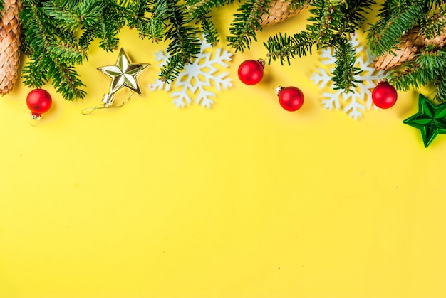 Christmas yellow background with fir tree branches, pine cones and christmas tree balls copy space above frame