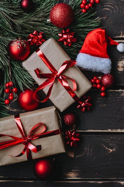 Christmass flatlay gift boxes,red christmas tree toys,santa hat\
and spruce brance on wooden backgro