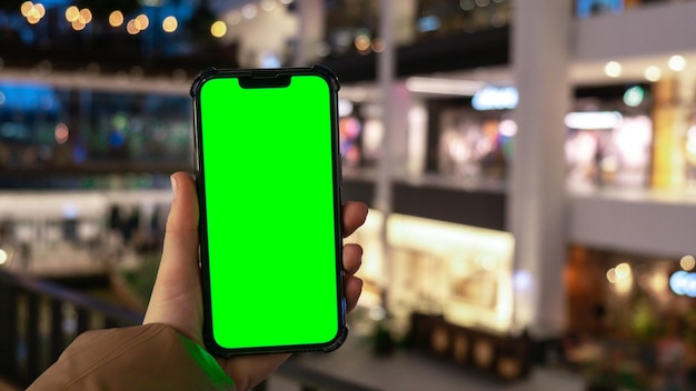 Chroma key primo piano della mano della donna tiene lo smartphone in verticale con schermo verde nel centro commerciale del centro commerciale grande magazzino shopping online modello di gadget