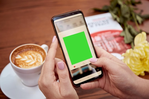 Chroma key mobile phone screen in woman39s hand and cup of coffee on the table Top view Education working freelance concept High quality photo