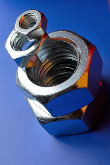 Chrome plated, metal nuts of different sizes, highlighted in different colors, laid out on a blue background.