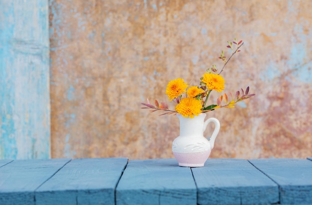 Chrysanthemum flowers in jug on background old wall