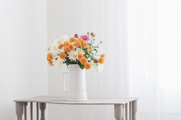 Chrysanthemum flowers in white jug in white interior