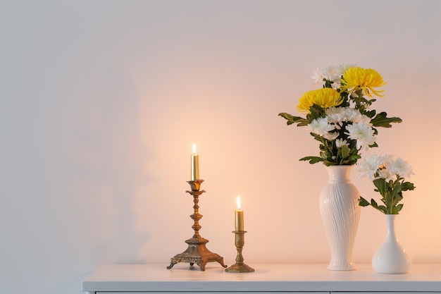 Chrysanthemums flowers in vases and burning candles on white interior