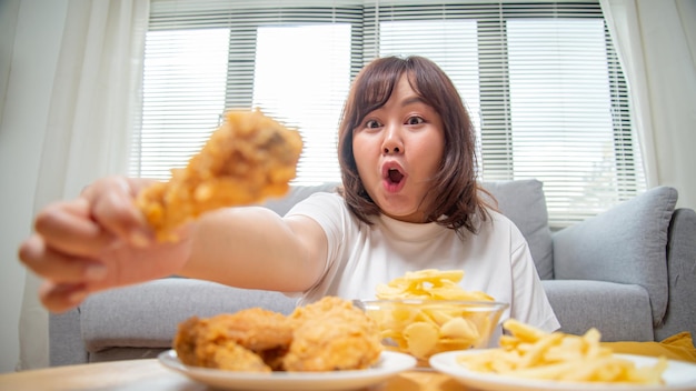 La donna asiatica paffuta esprime felicità quando si mangiano patatine fritte di pollo e snack di patate