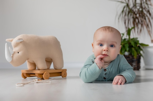 chubby baby in a green jumpsuit is sitting on the floor and playing with a wooden toy on a string