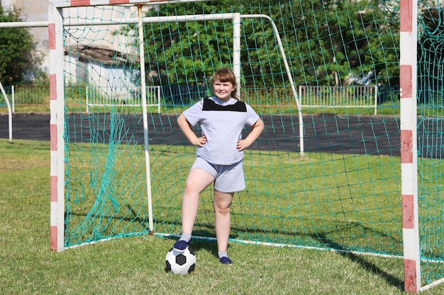 ぽっちゃりした女の子がサッカーのゲートに立って、足でボールを押す