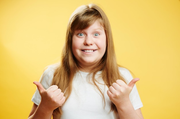 Chubby redhead teen girl showing thumbs up standing on a yellow background