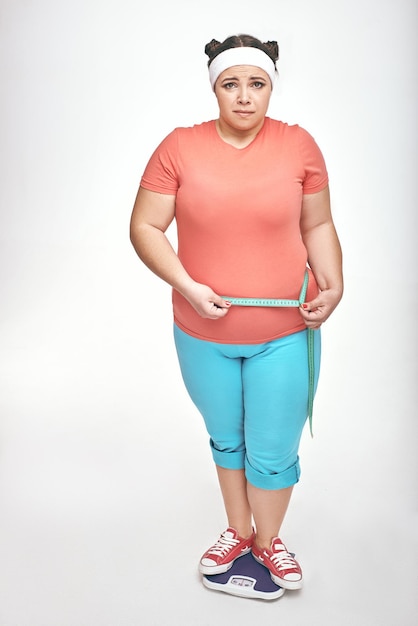 Chubby woman is measuring her belly on white background