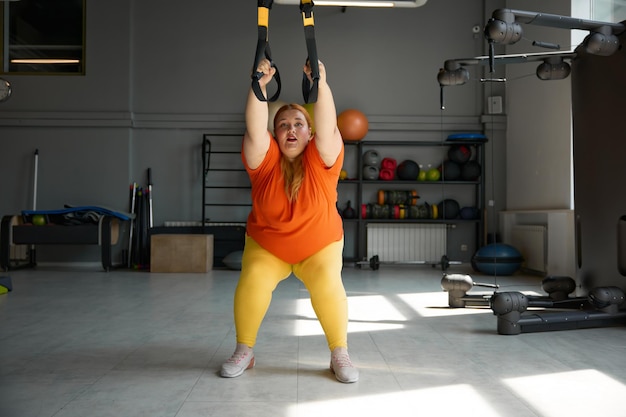 Chubby woman working in bodyweight training program using trx loops. Total resistance exercises for weight lost