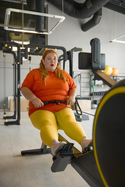 Photo chubby woman working hard on training machine at gym obesity struggle and sports concept