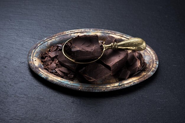 Chunks chocolate on metal tray and brass scoop on a black slate background