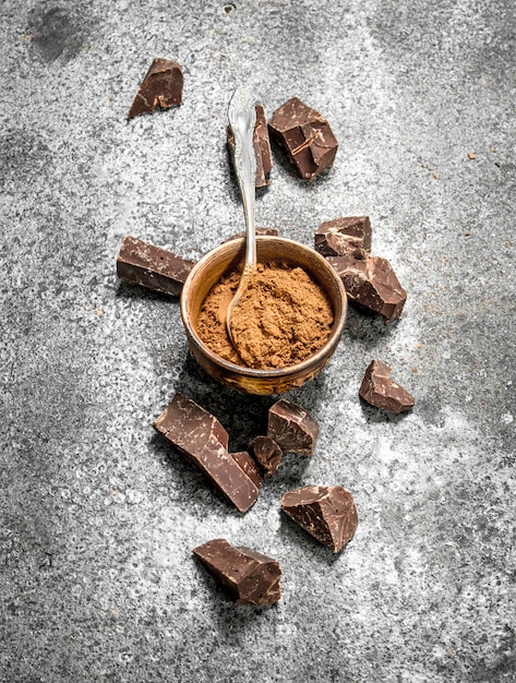 Chunks of chocolate with cocoa powder. On a rustic table.