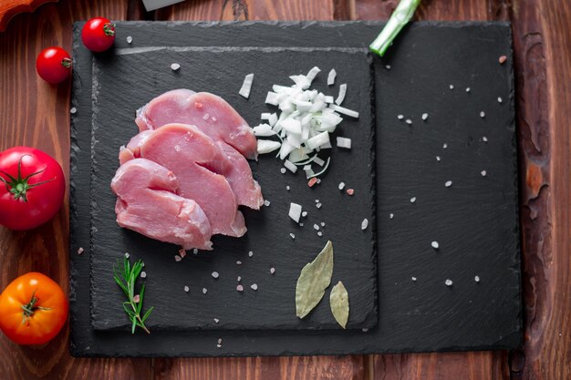 Photo chunks of sliced raw turkey meat, chopped onions, on a black slate background.