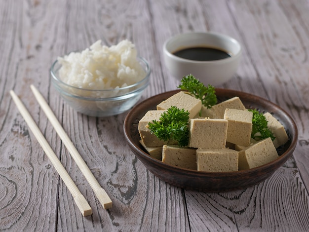 Chunks of tofu, rice, soy sauce and chopsticks on a wooden table. Soy cheese. Vegetarian product.