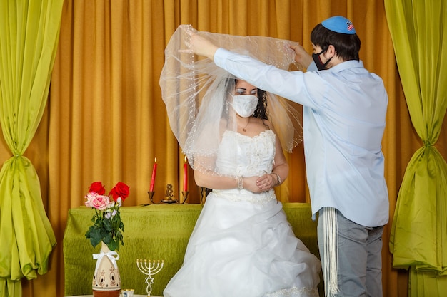 During the chuppah ceremony in the synagogue, the masked groom lifts the veil from the bride's face