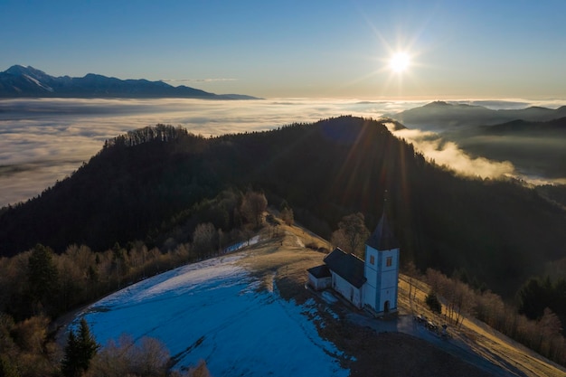 Foto chiesa di san primoz e felicijan all'alba sopra le nuvole alpi giulie jamnik slovenia europa veduta aerea