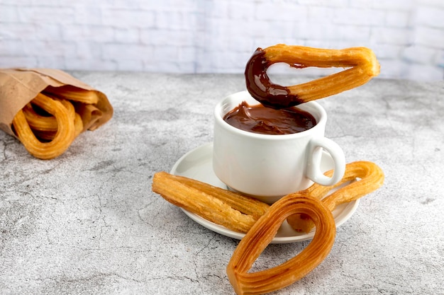 Churro는 전형적인 스페인식 아침 식사인 회색 돌 배경에 핫 초콜릿 한 잔에 담그고 있습니다.