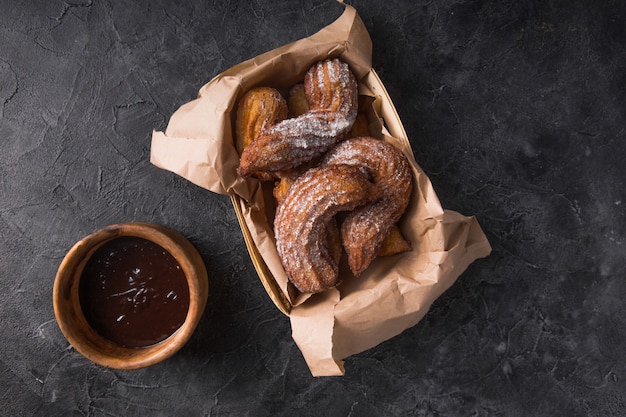 Churros in een papieren zak met suiker en chocoladesaus op zwart