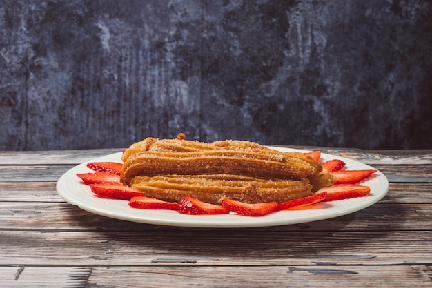 Churros met aardbeien op een witte plaat op een houten tafel.