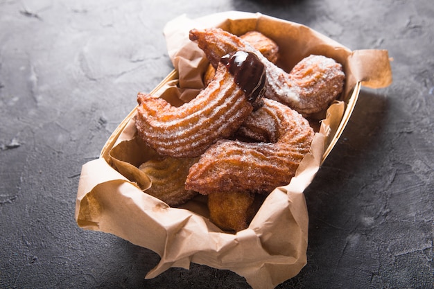 Churros in a paper bag with sugar and chocolate sauce on black