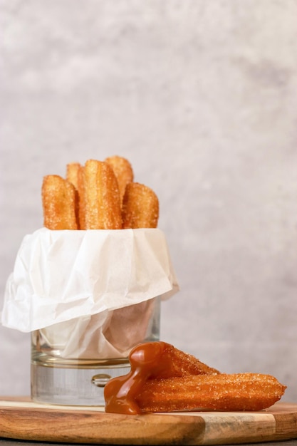 Churros with sugar and caramel sauce in a glass, grey table with copy space