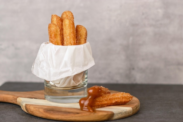 Churros with sugar and caramel sauce in a glass, grey table with copy space