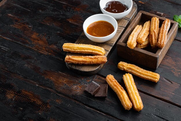 Churros con zucchero e salsa al cioccolato, sul vecchio fondo della tavola in legno scuro con spazio per testo, copyspace