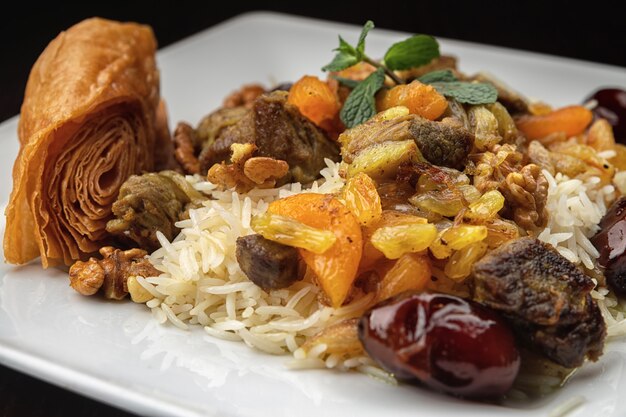 Chyhyrtma pilaf with lamb meat, dried fruits, dates and walnuts, on a white plate