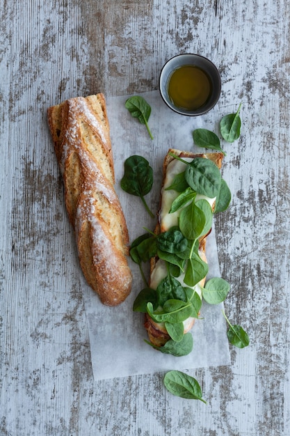 Ciabatta broodje met pesto, kruiden, prosciutto, salami, worst, mozzarella en spinazie op grijs hout, bovenaanzicht