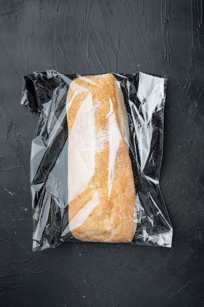 Ciabatta in een plastic zak, op zwarte achtergrond, bovenaanzicht plat lag