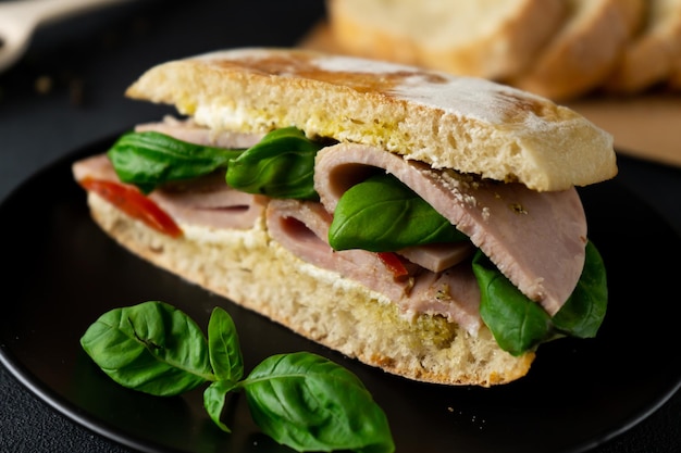 Ciabatta Sandwich with Ham Pesto sauce Tomatoes Basil on a black background Food Food backgroun