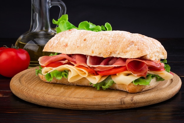 Ciabatta sandwich with lettuce prosciutto and cheese on wooden board