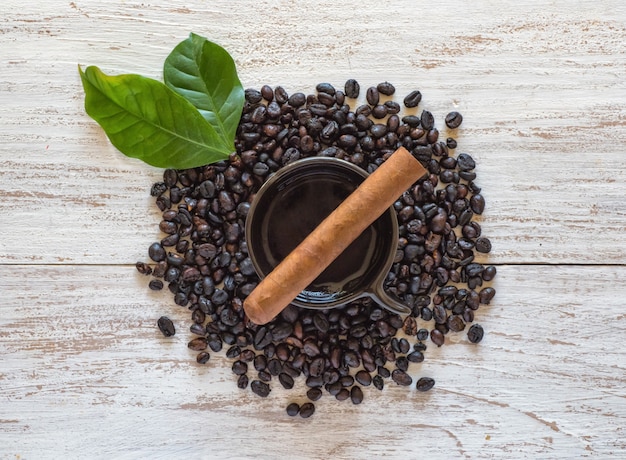 Cigar on a cup of black coffee with coffee beans.