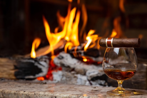 Cigar and a glass of cognac on the background of the fireplace