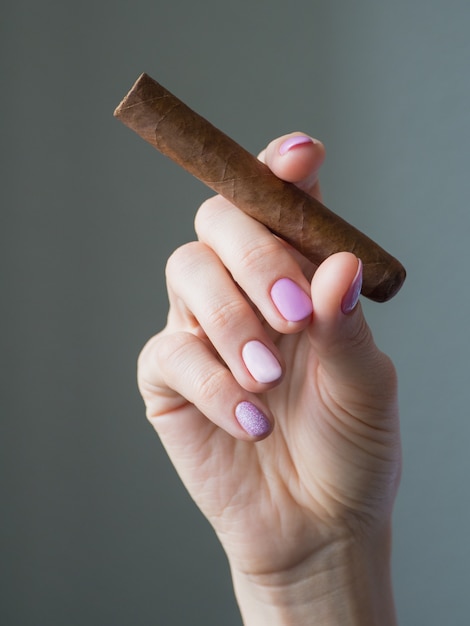 Cigar in woman hand, photo on gray table