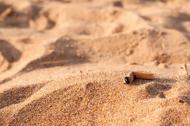 A cigarette butt is lying on the beach against the background of sand dunes with a place for text on a blurry background