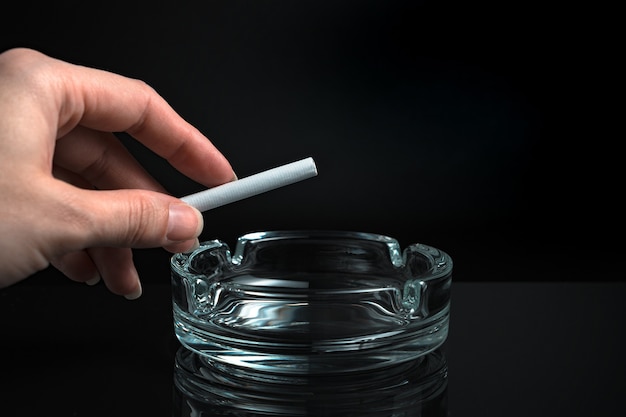 Cigarette in hand over an ashtray on a black background.