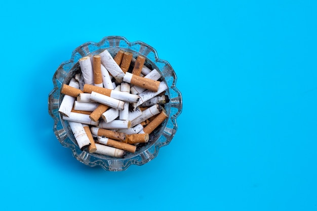 Cigarettes buds in a transparent ashtray on blue.