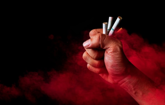 붉은 연기와 어두운 배경에 있는 남자의 손에 있는 담배