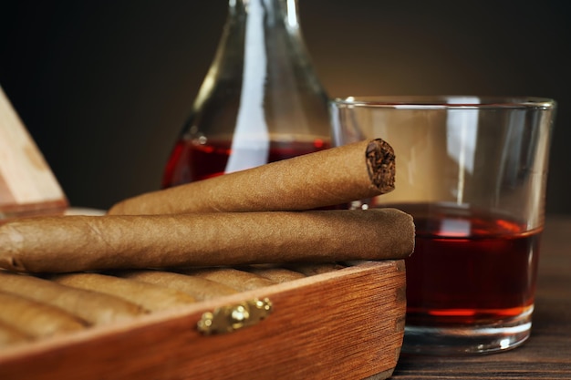 Cigars with glass of cognac on wooden table closeup