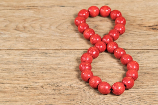 Cijfer 8 bekleed met rode houten kralen op een oude houten tafel