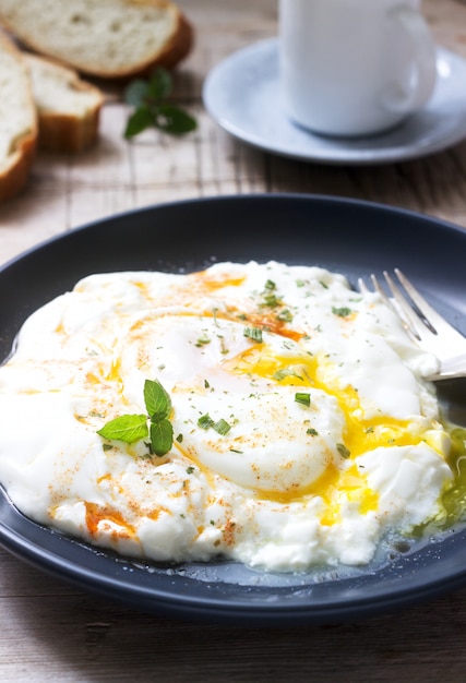 Cilbir, poached egg in yogurt with spiced butter and herbs, served with bread and a cup of coffee.