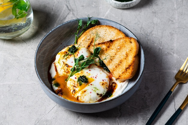 Cilbir or Turkish Eggs. dish served as mezze: poached eggs topped over herbed greek yogurt, then drizzled with hot spiced paprika olive oil. Turkish breakfast in a grey bowl on marble background