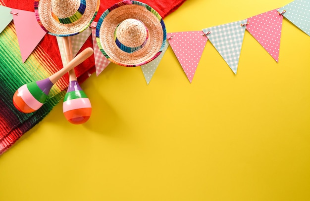 Cinco de mayo holiday background made from maracas mexican\
blanket stripes or poncho serape and hat on yellow background