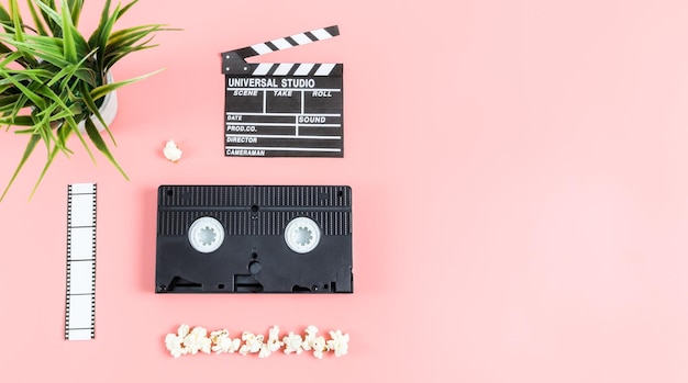 Cinema clapperboard film strip videotape popcorn and flowerpot on the left against a pink