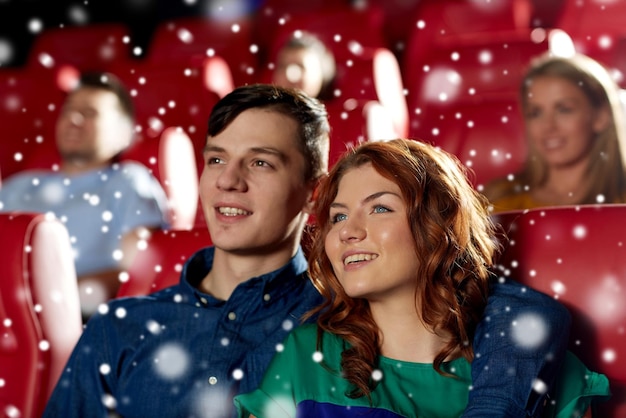 Photo cinema, entertainment and people concept - happy couple watching movie and hugging in theater over snowflakes