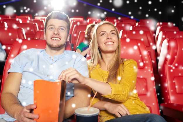 映画、娯楽、人のコンセプト – 幸せな友人やポップコーンとレモネードの飲み物を持つカップルが、雪片のある劇場で映画を見ている