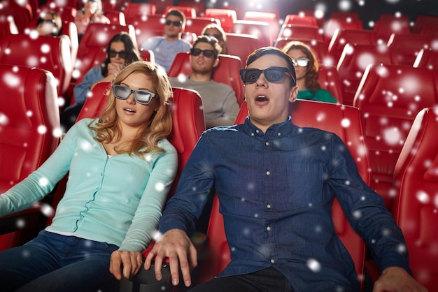 cinema, technology, entertainment and people concept - scared friends or couple with 3d glasses watching horror or thriller movie in theater with snowflakes