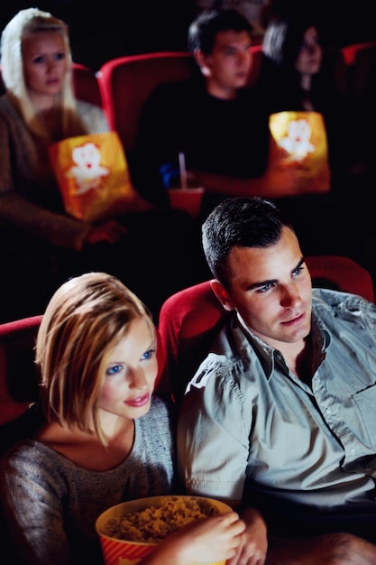 Cinema watching and couple with popcorn film and eating on romantic date together Movie night man and woman in theater with snacks entertainment and sitting in auditorium to relax at premier